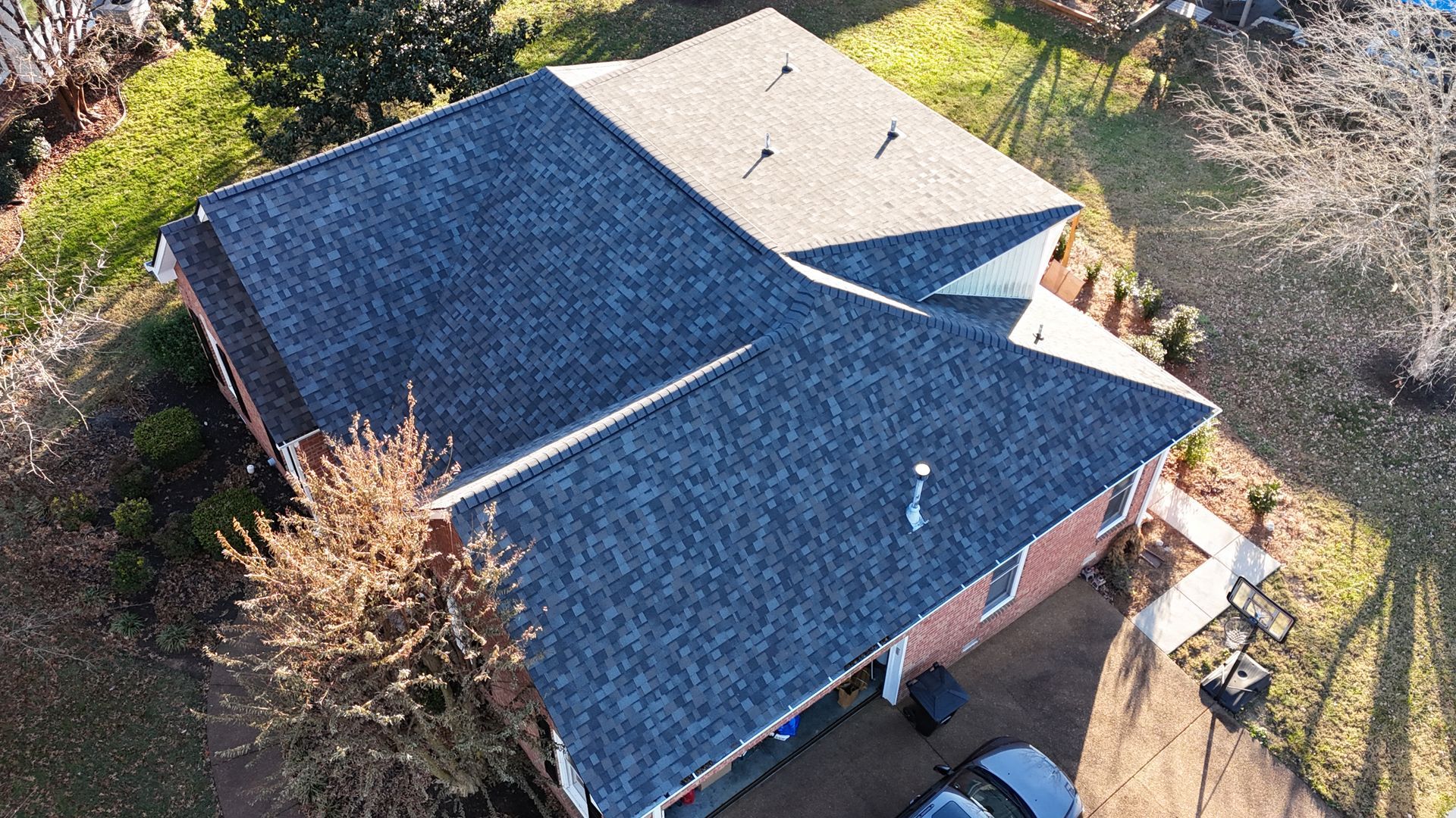 Aerial view of a residential house with a dual-colored roof featuring dark gray and light tan shingles on a sunny day.