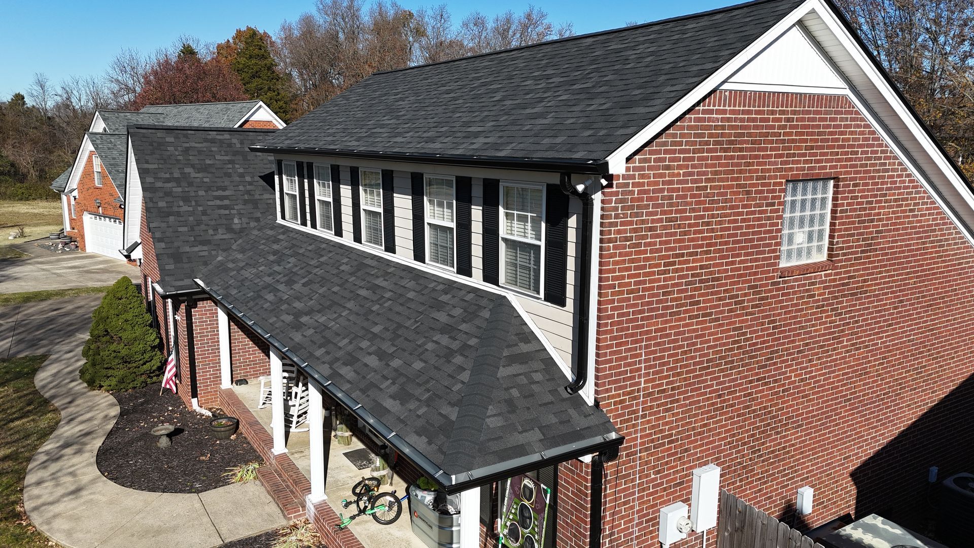 An aerial view of a two-story red brick house with a newly installed dark shingle roof, white trim, and a front porch.