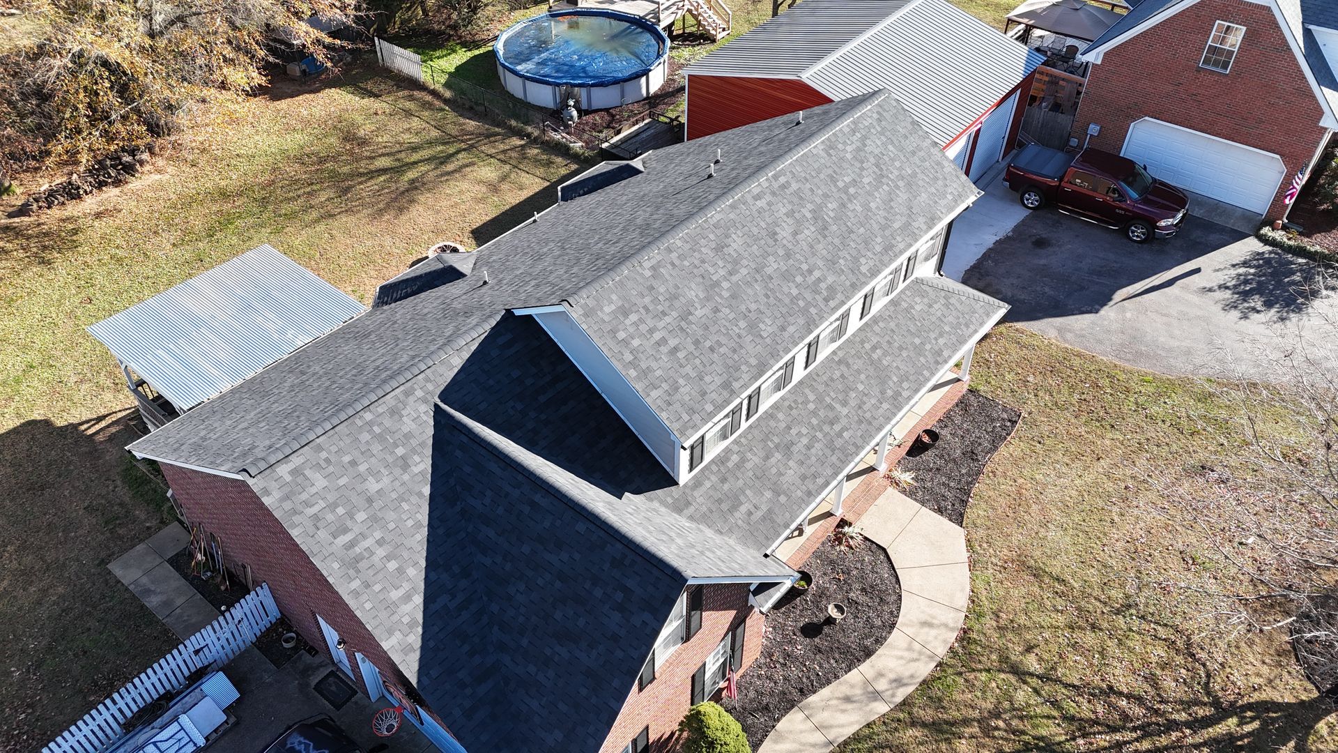 Aerial view of a residential brick house with a dark gray shingled roof, an adjacent pool, and a red detached garage.