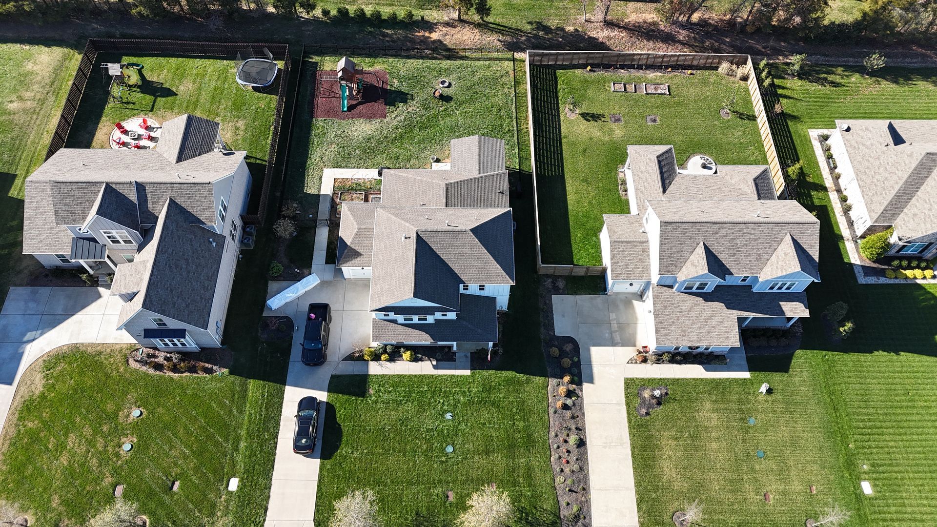 Aerial view of four residential suburban homes with driveways and backyards separated by fences on a sunny day.