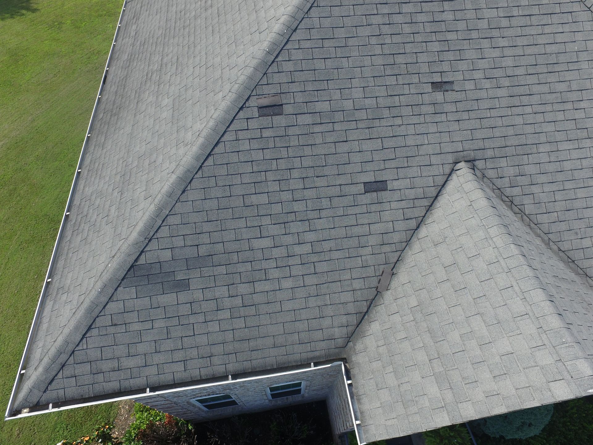 A high-angle aerial view of a gray asphalt shingle roof with visible patches of different colored shingles.