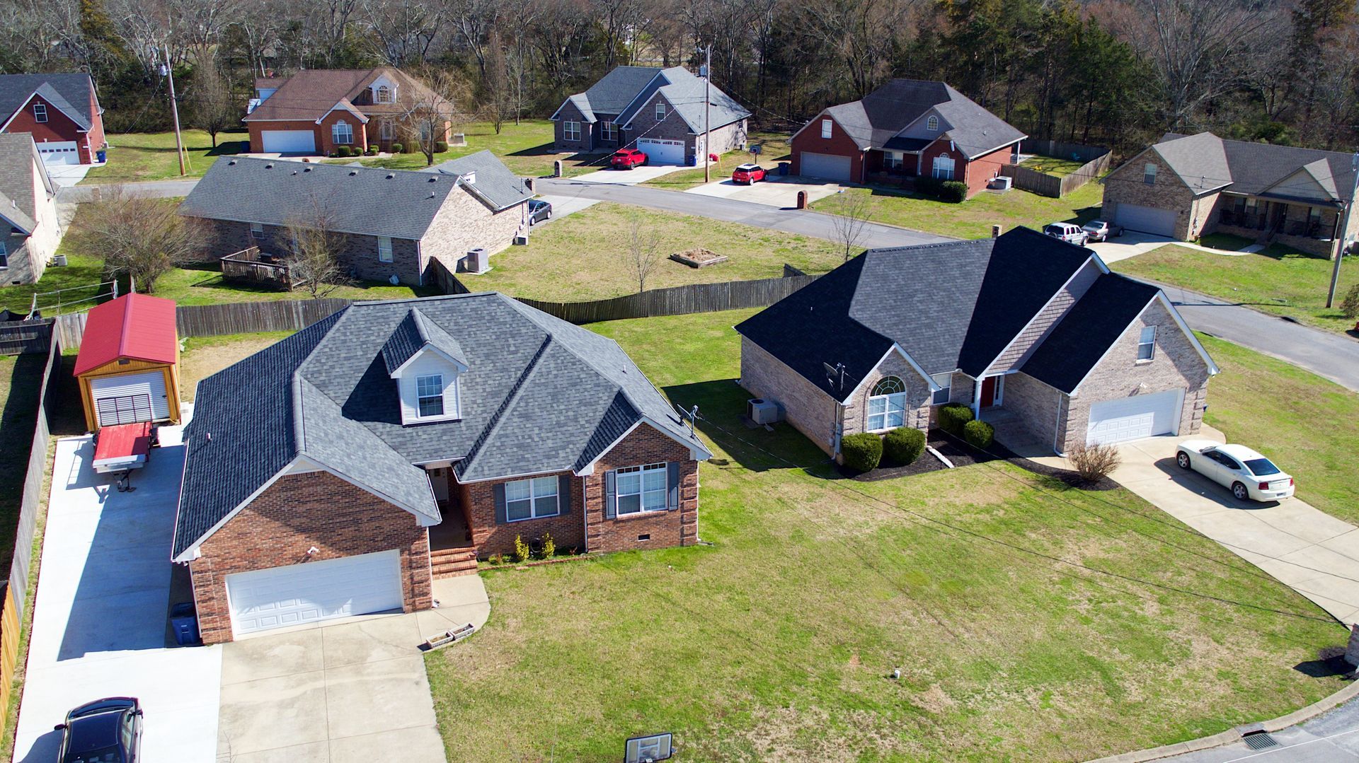 Aerial view of suburban brick houses on a sunny day with green lawns and paved driveways.