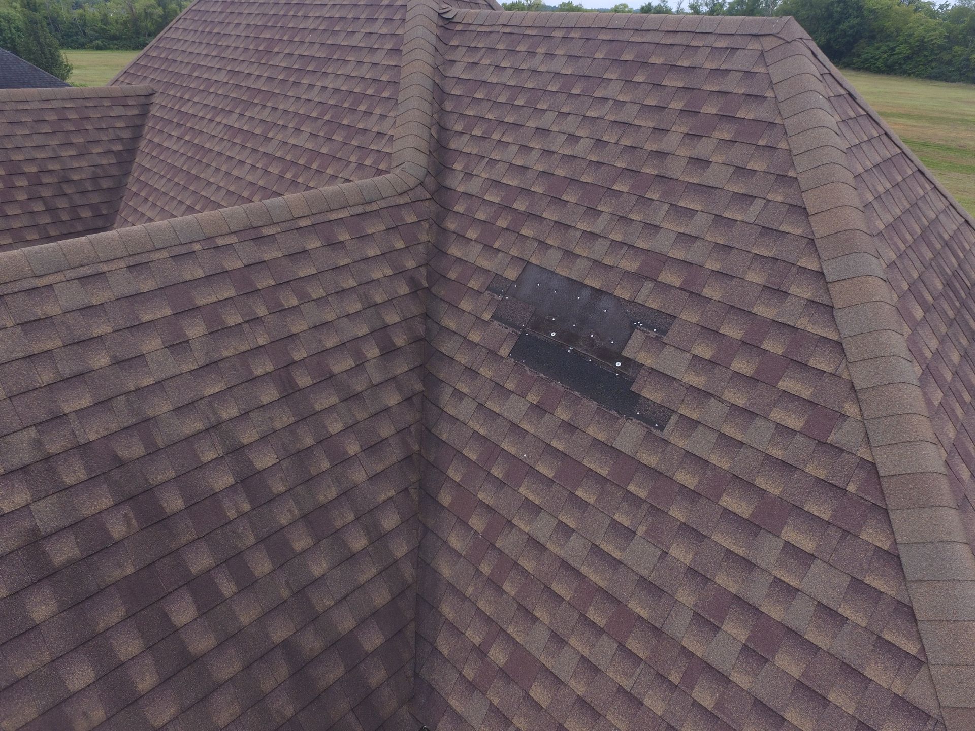 A brown shingled roof features a patch of exposed black underlayment with visible nails where shingles are missing.
