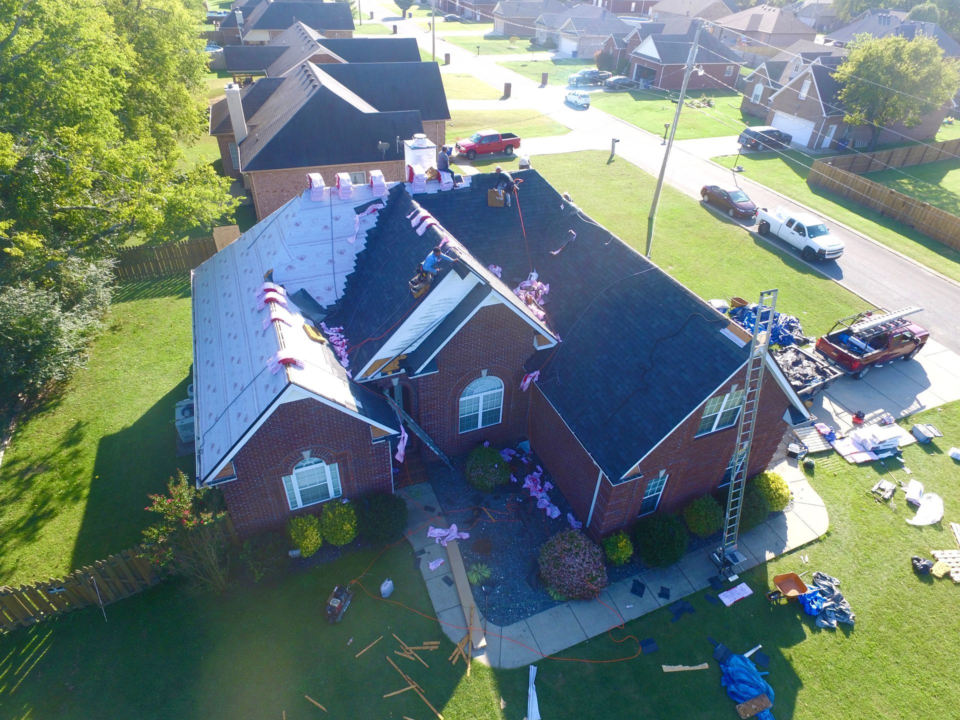An aerial view of a brick house under construction, with sections of the roof covered in white underlayment and shingles.