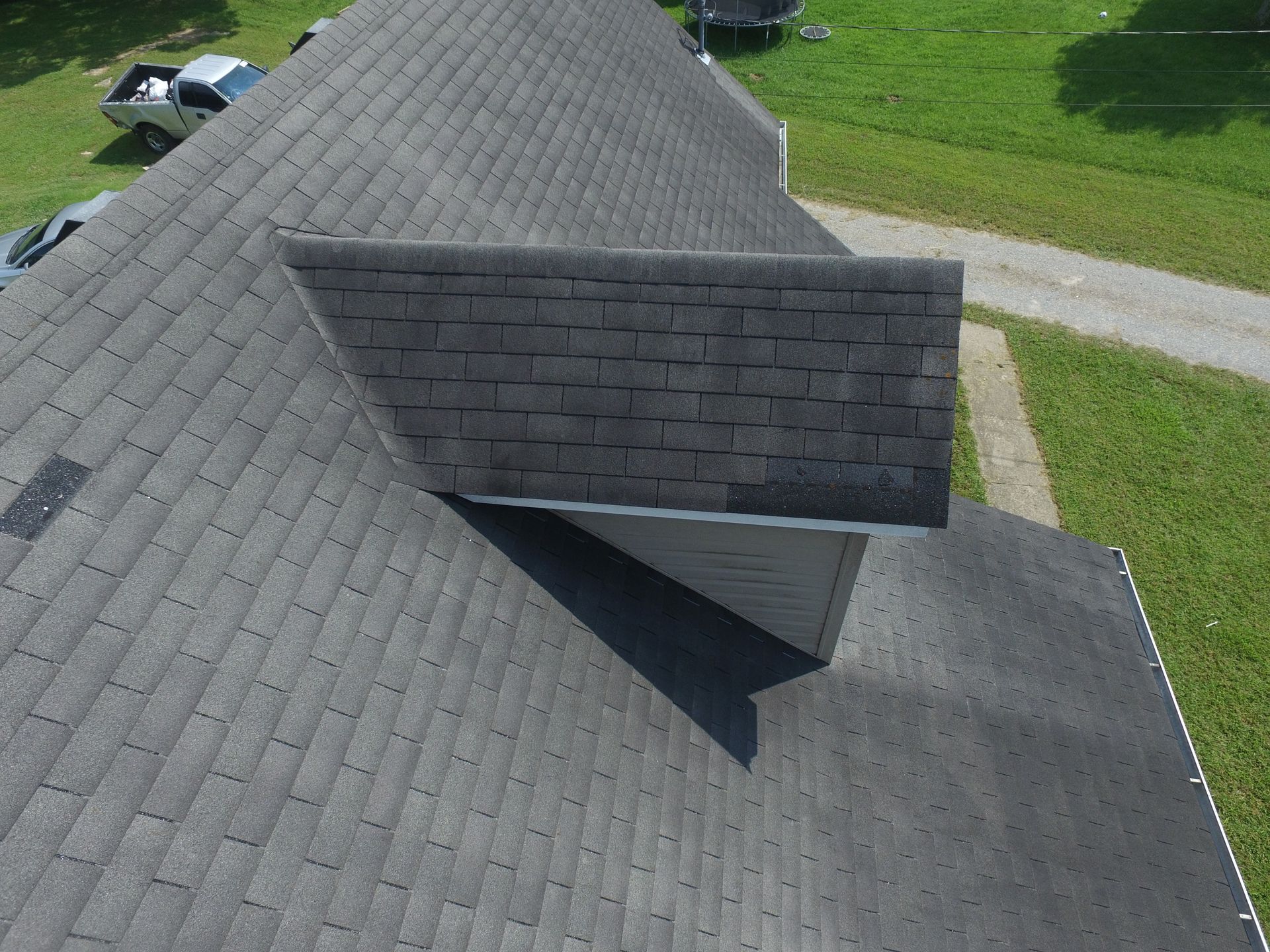 An aerial view of a gray asphalt shingle roof featuring a dormer projecting from the main roof slope.