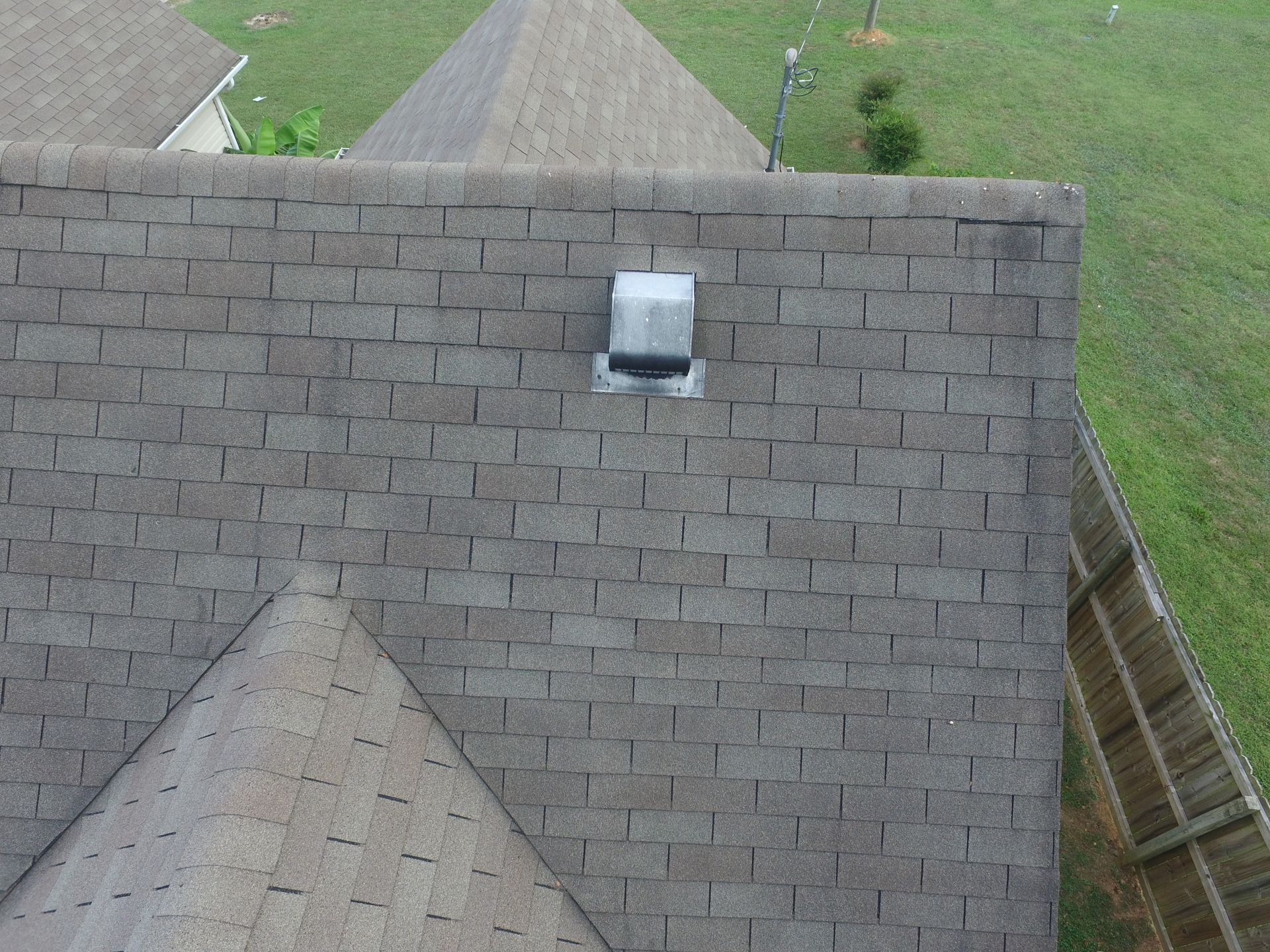 A gray asphalt shingle roof with a square ventilation hood installed near the peak, viewed from above.