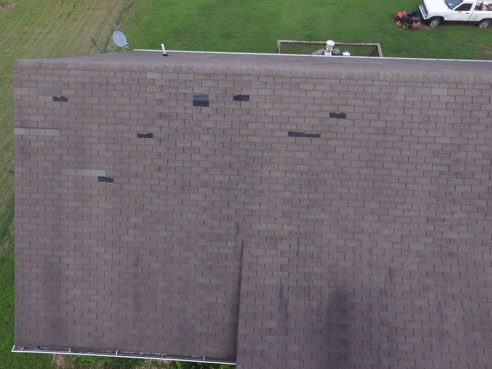 An aerial view of a brown shingled roof with several black patches indicating recent repairs.