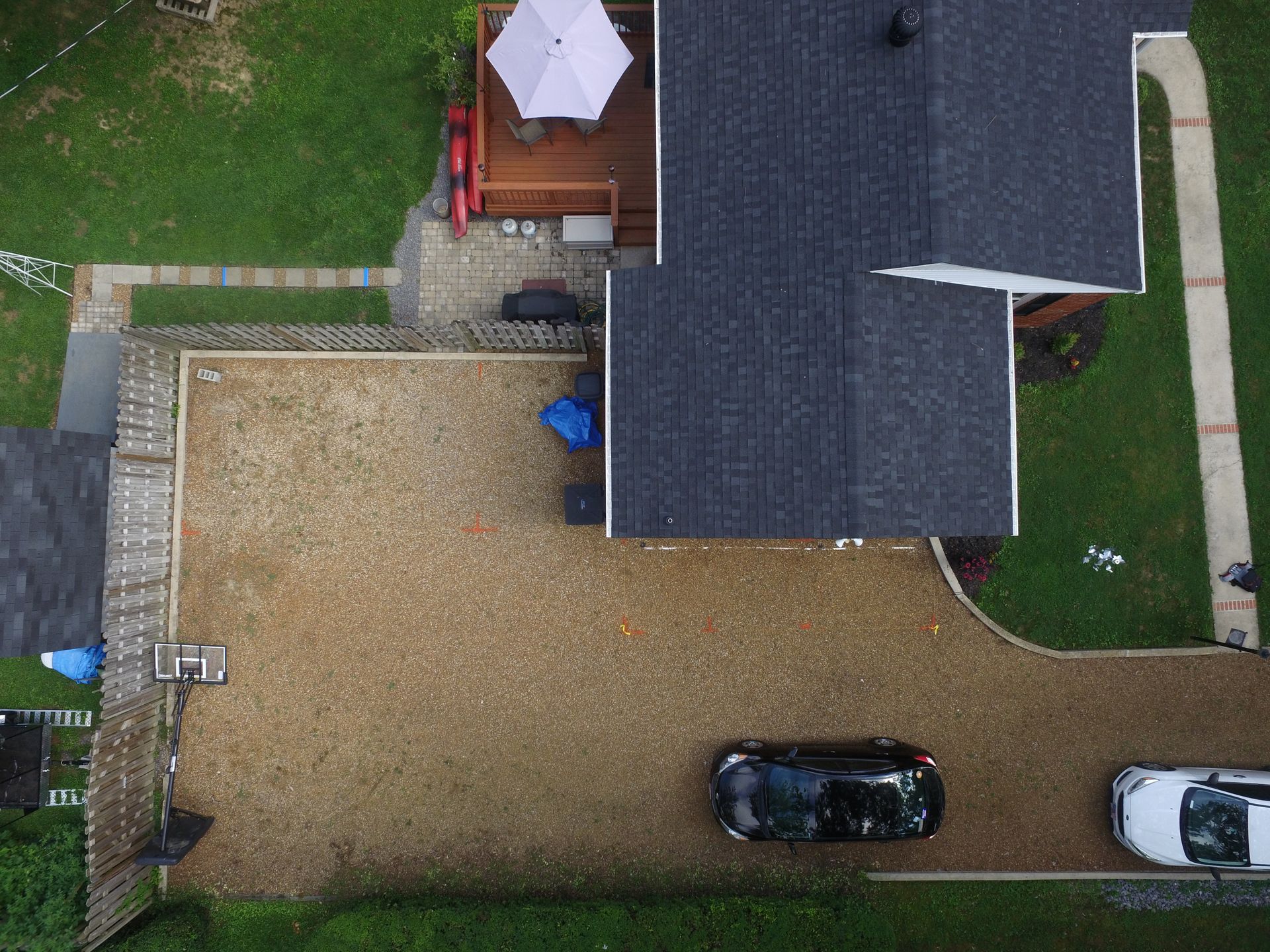 Aerial view of a gravel driveway and parking area next to a house with a dark roof and small deck.