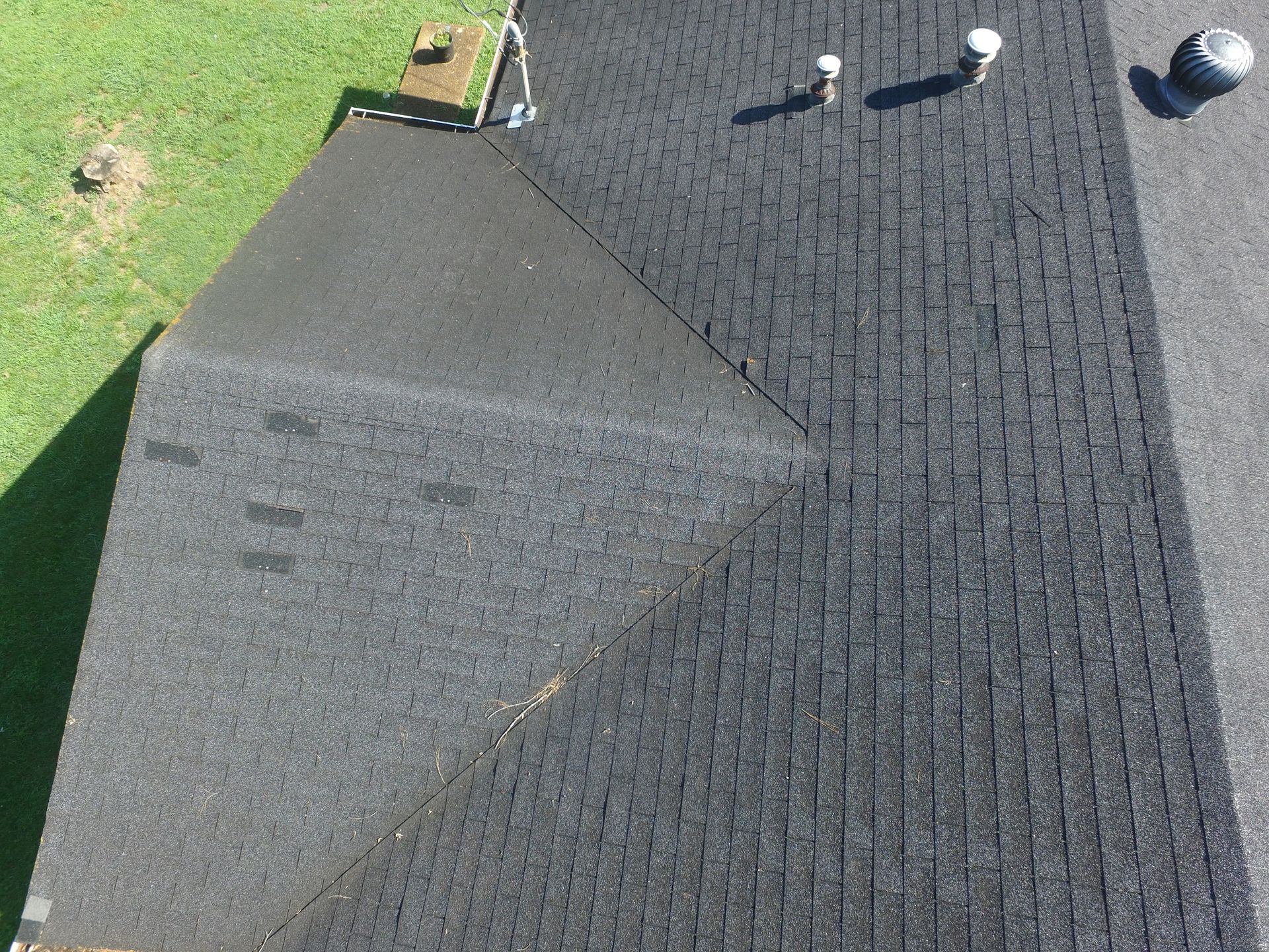 An aerial view of a dark asphalt shingled roof with a prominent triangular section and several roof vents.