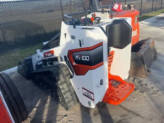 A white and orange Bobcat MT100 mini track loader parked outdoors on a paved surface.