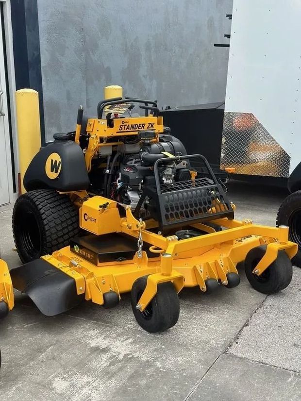 A yellow Wright stand-on commercial lawn mower parked on concrete.