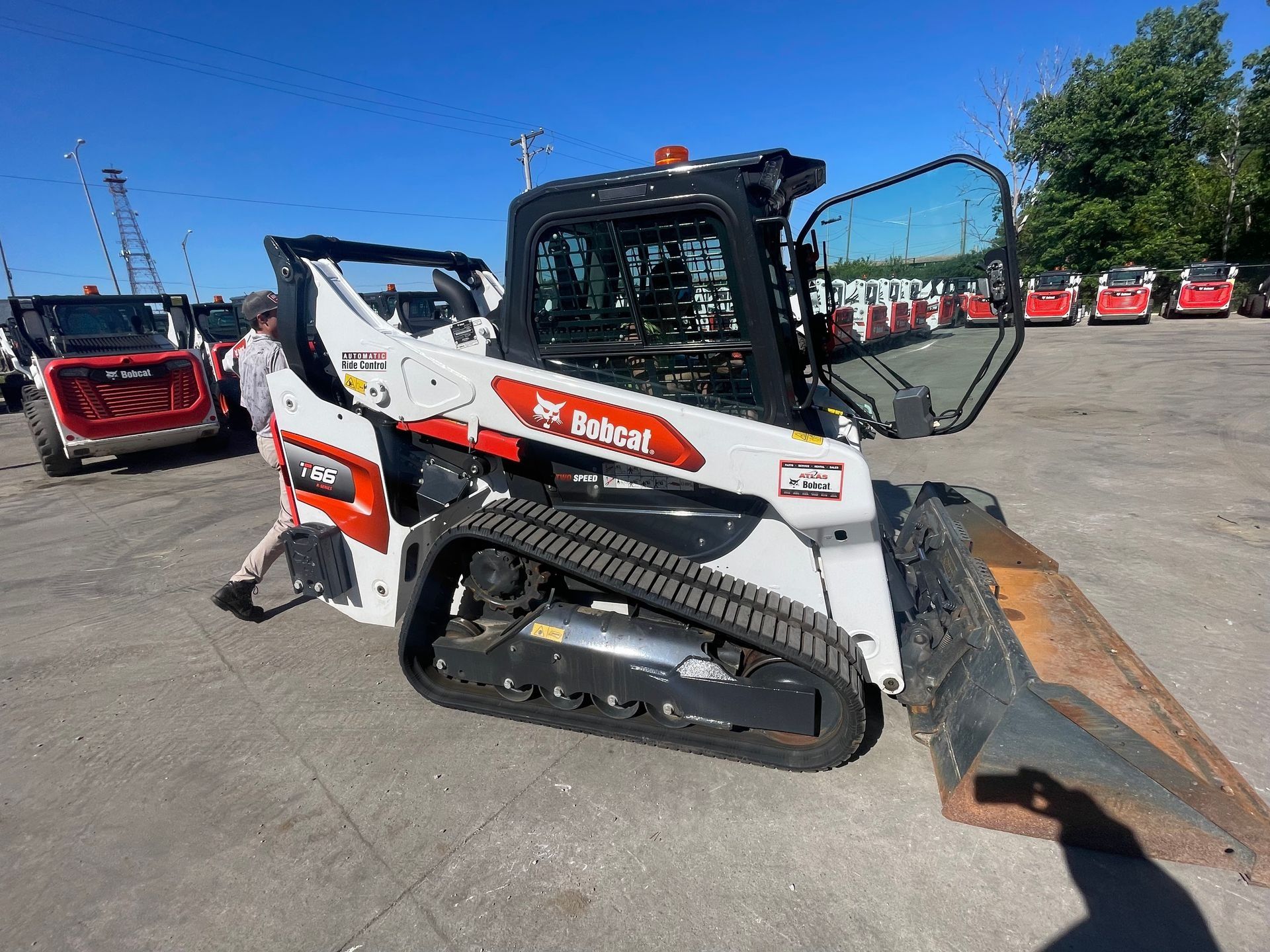 A white Bobcat T650 compact track loader parked outdoors, with a person standing next to it in a equipment lot.
