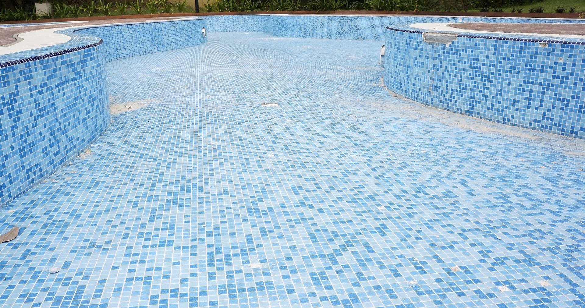 Empty swimming pool lined with small, square blue and white mosaic tiles.