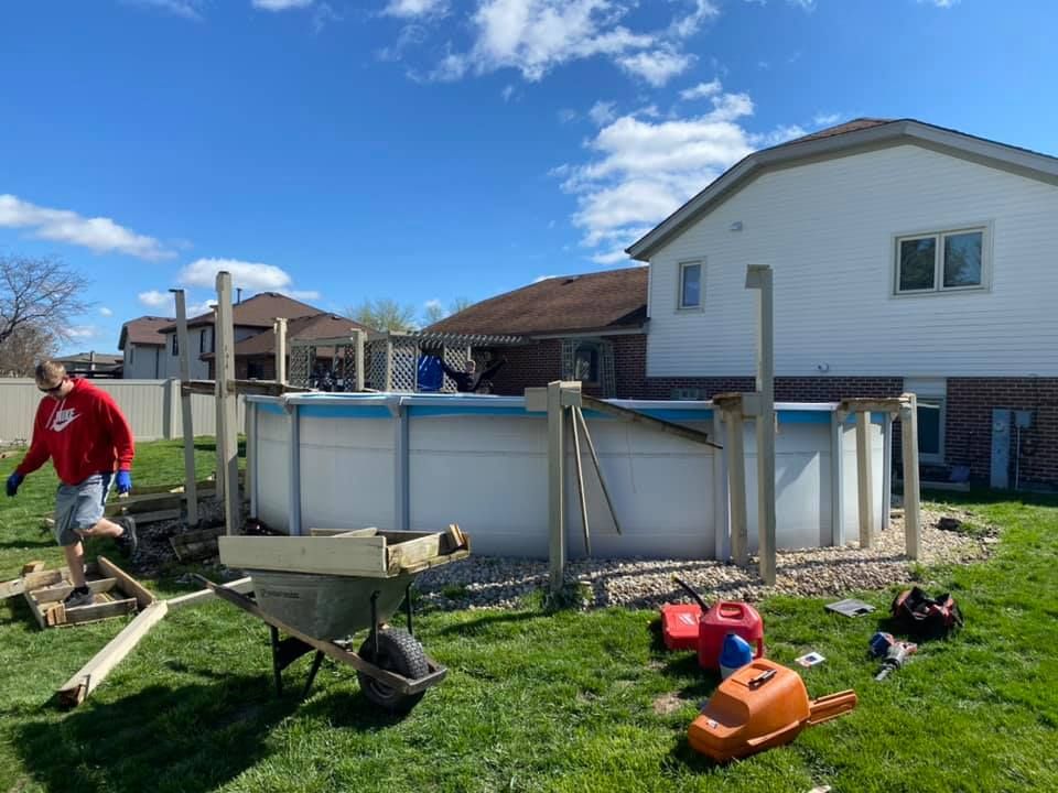 A person in a red sweatshirt works near a partially dismantled above-ground swimming pool in a residential backyard.