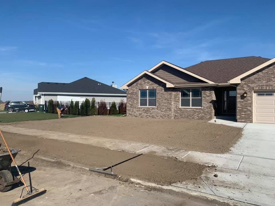 A brown brick house with a newly graded dirt yard under a clear blue sky, next to a sidewalk and a neighboring house.