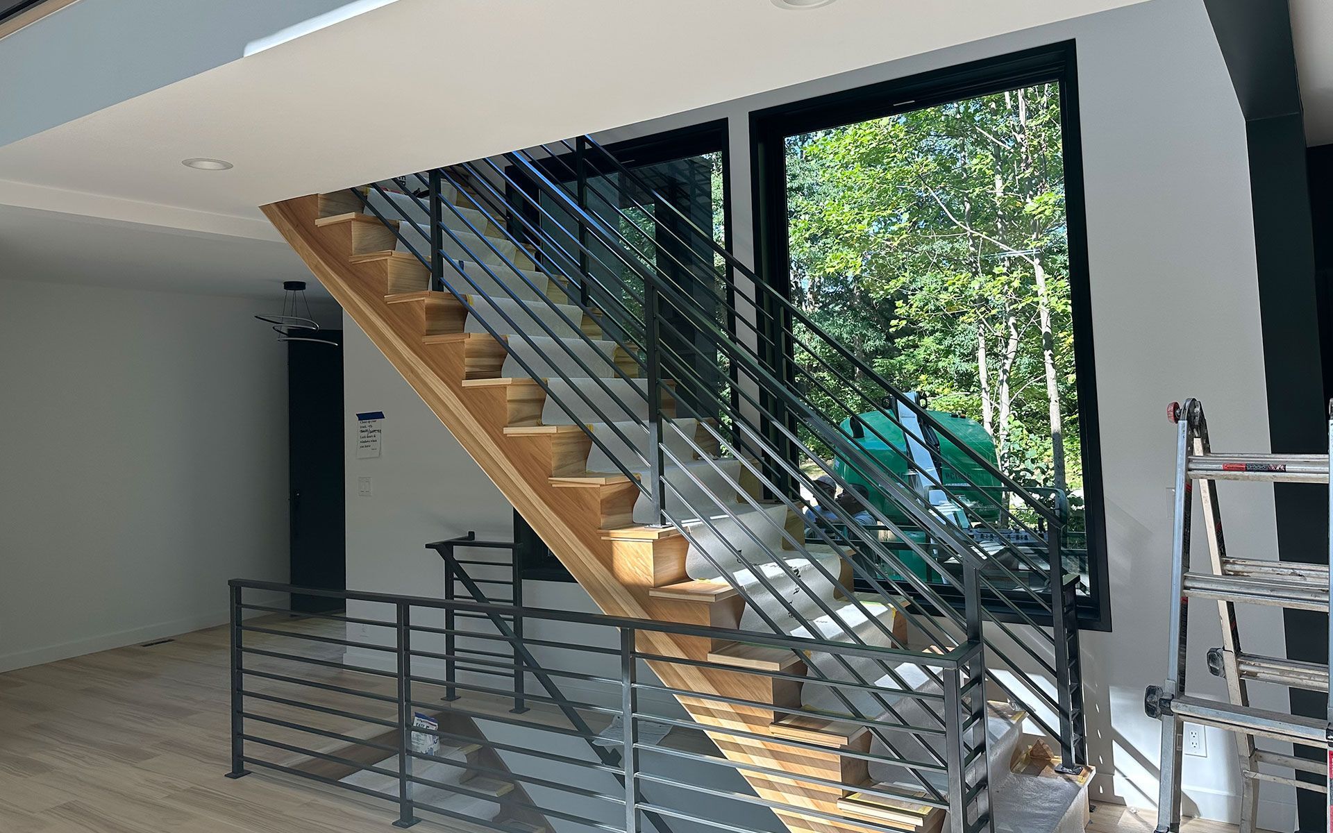 A wooden staircase with a metal railing in a room with a large window.