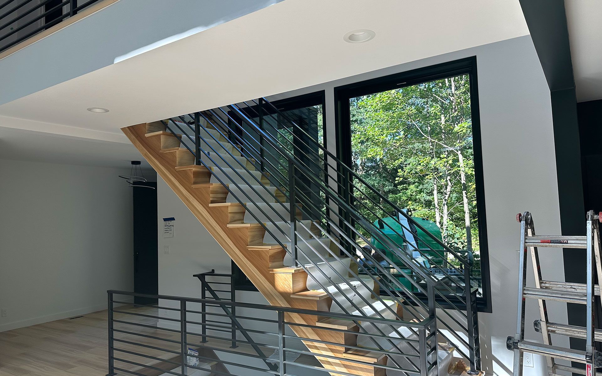 A wooden staircase with a metal railing in a house with a large window.