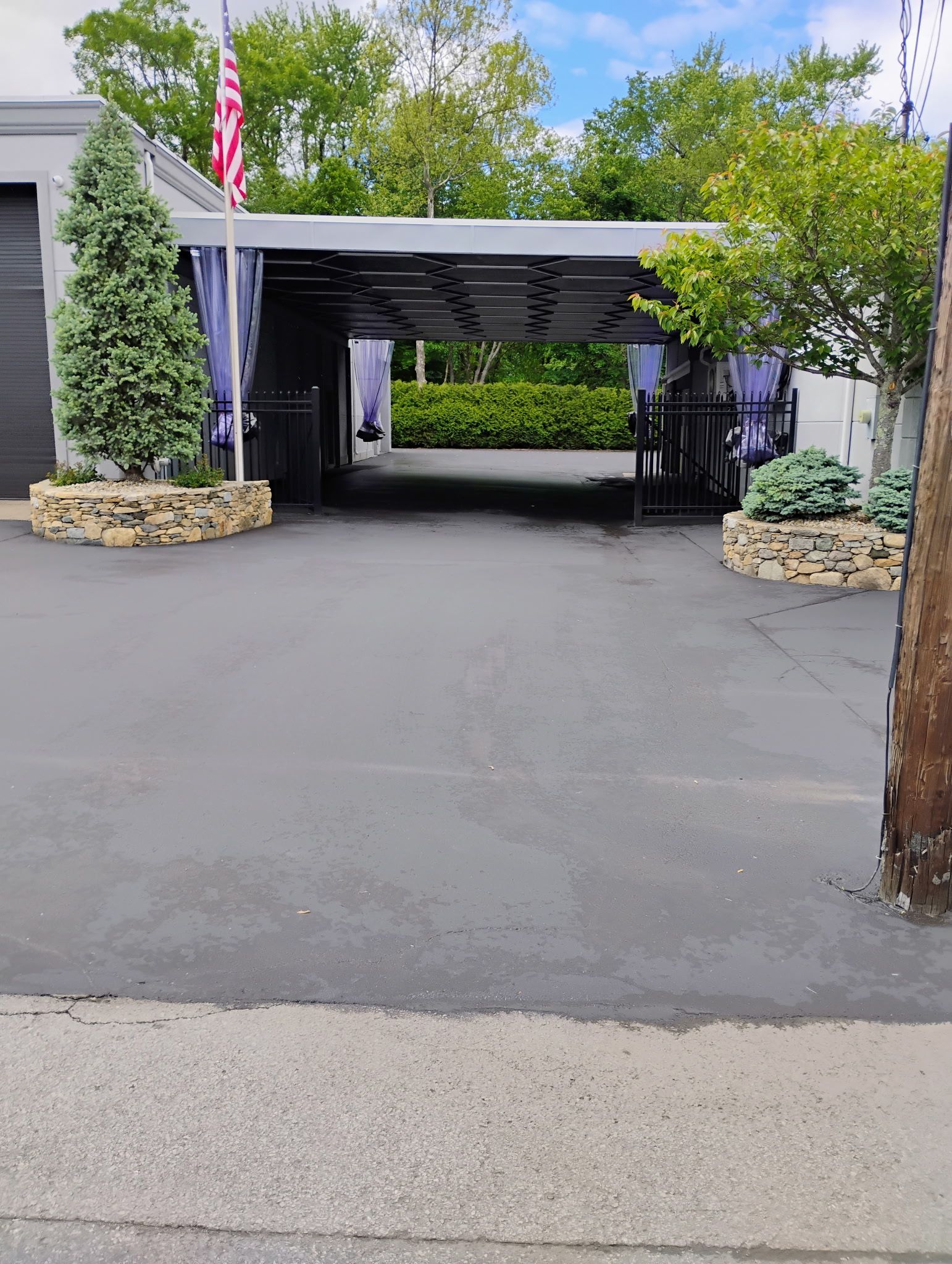 Driveway leading to a covered carport beside a house, with trees and stone planters on both sides.