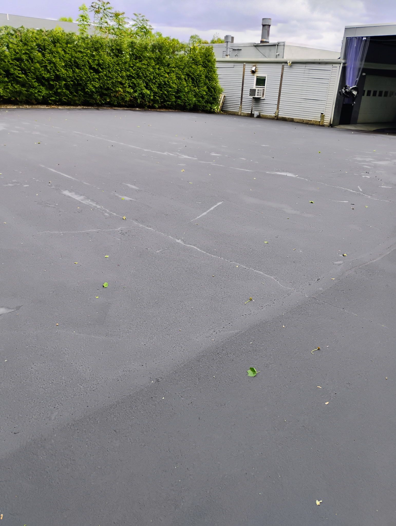 Empty gray rooftop with green hedge and utility structures in the background