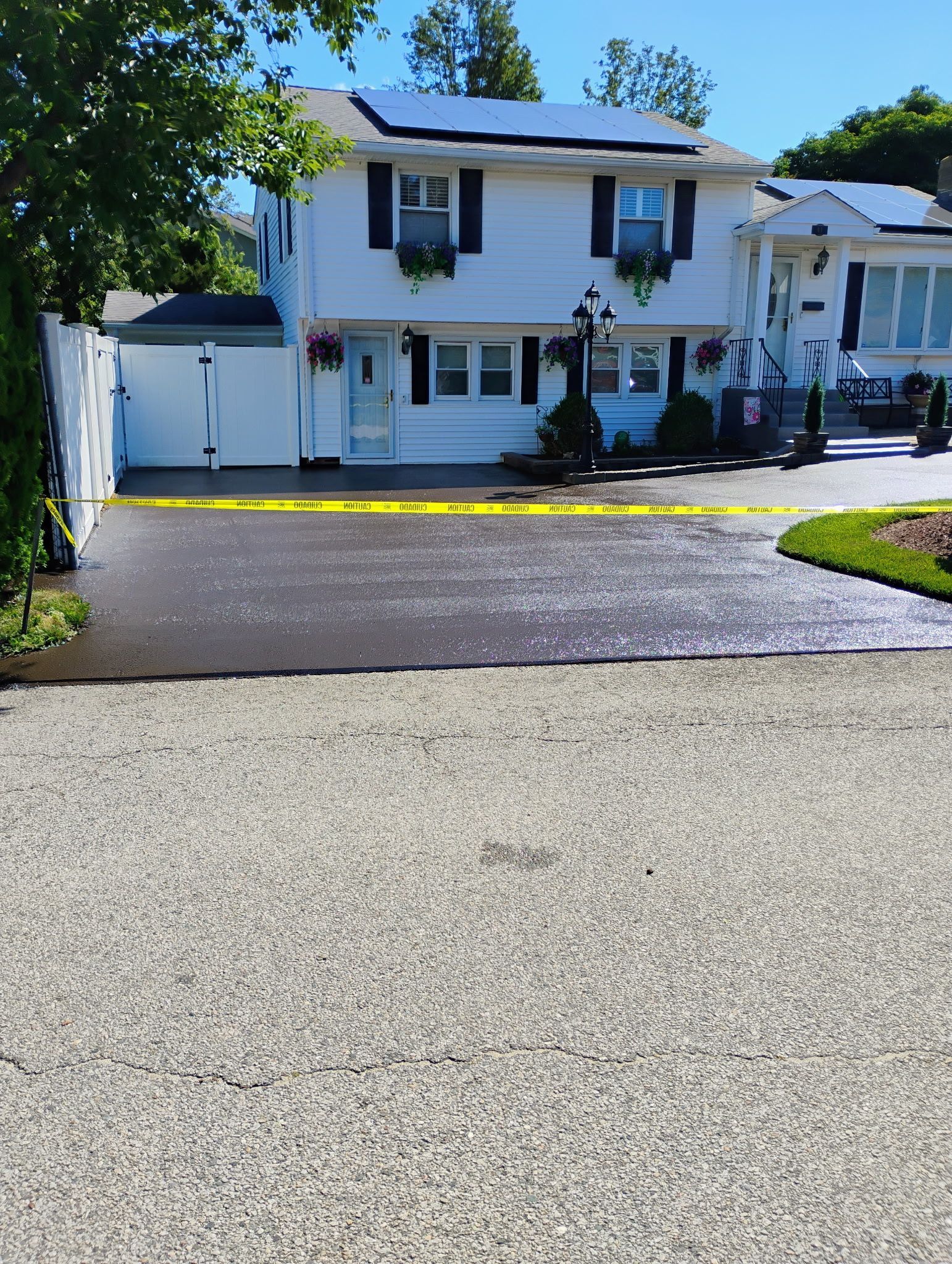 White two-story house with black shutters, driveway, and garage under a clear blue sky.