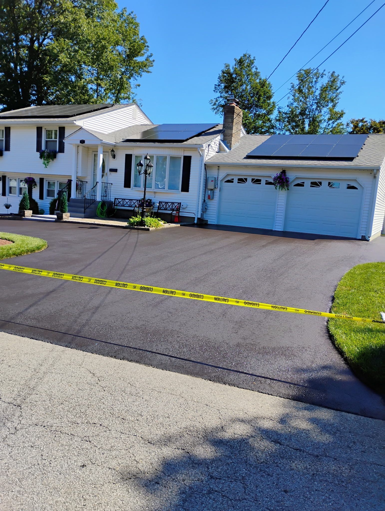 White house with blue garage doors, dark driveway, and solar panels under a clear blue sky.