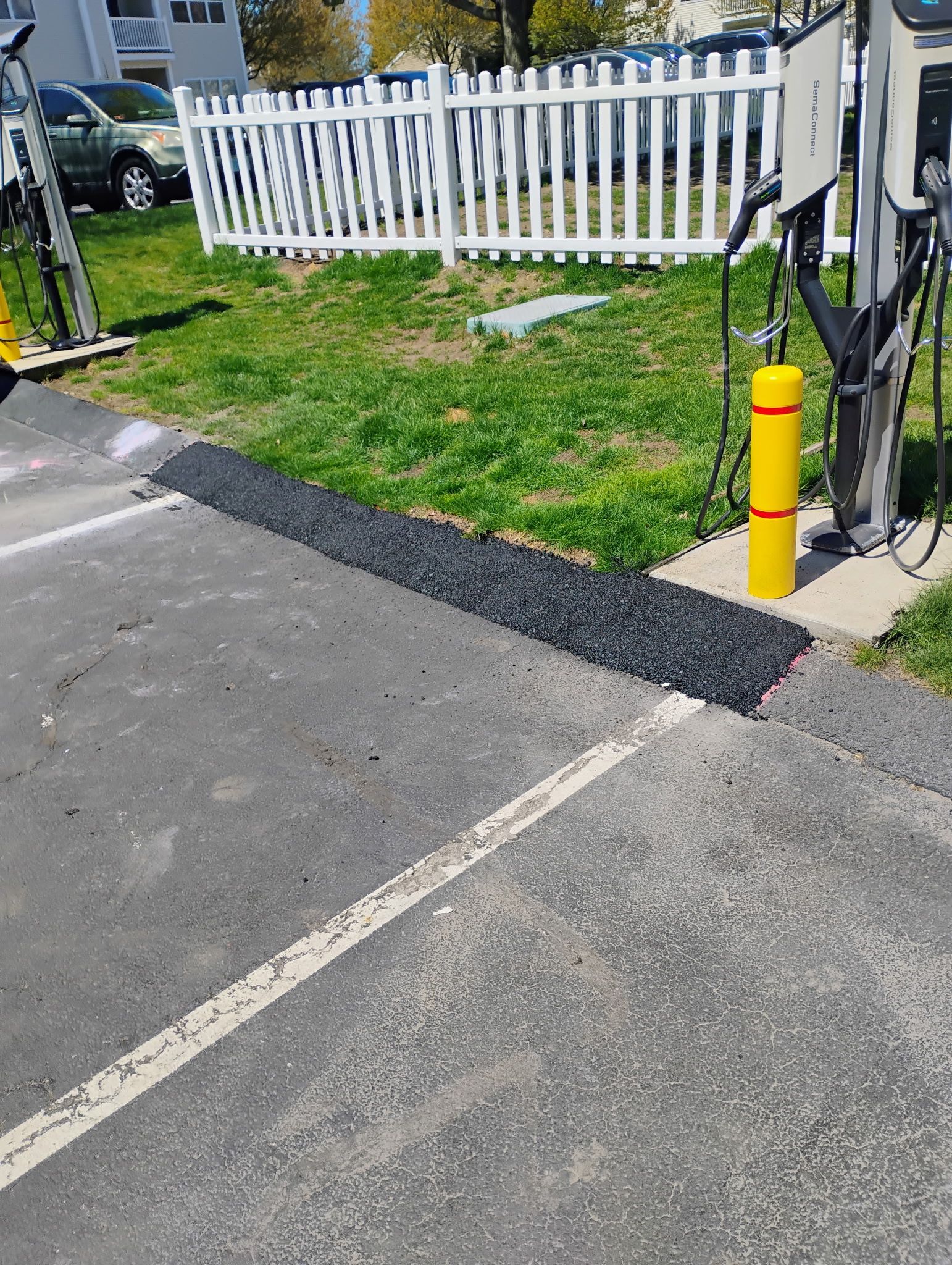 Small yellow bollard beside a driveway, with cables and a white fence in the background.