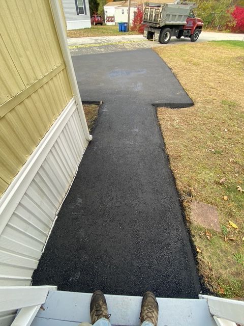 Freshly paved black asphalt walkway beside a yellow house, leading to a driveway and utility truck.