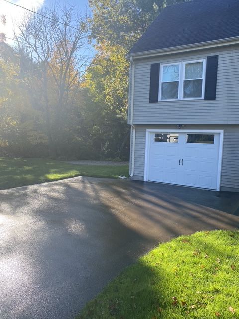 Sunlit suburban house with a garage, driveway, and green lawn beside trees