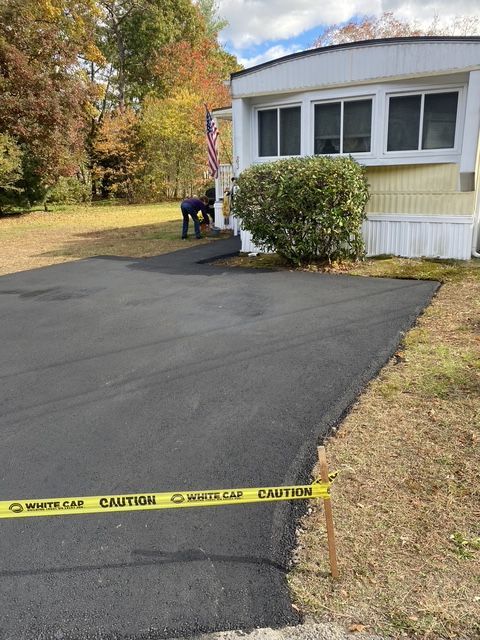 Freshly paved driveway beside a house, marked with caution tape; a person works near the side entrance.