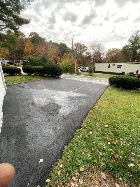 Wet residential driveway and road with parked cars, trees, and a cloudy autumn sky.