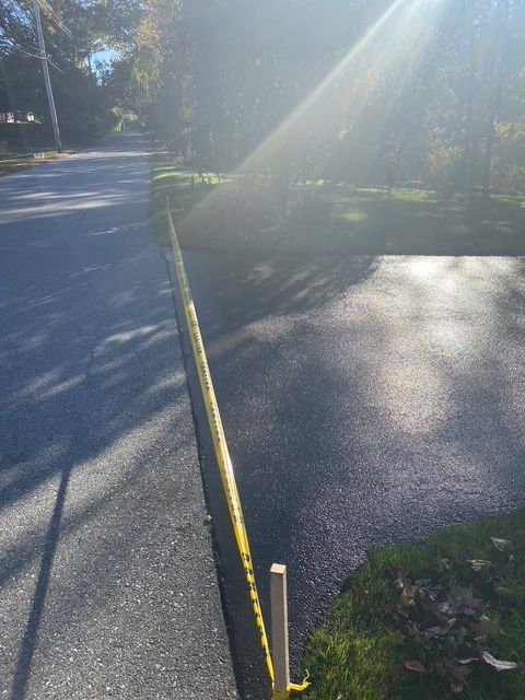 Sunny paved path beside a yellow handrail in a wooded park.