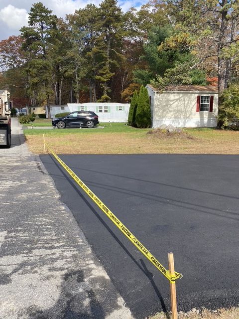 Yellow caution tape blocks a paved driveway beside a white shed and parked car in a wooded residential area