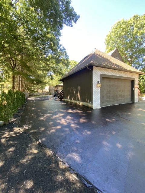 Detached gray garage with white trim and a closed door beside a tree-lined driveway