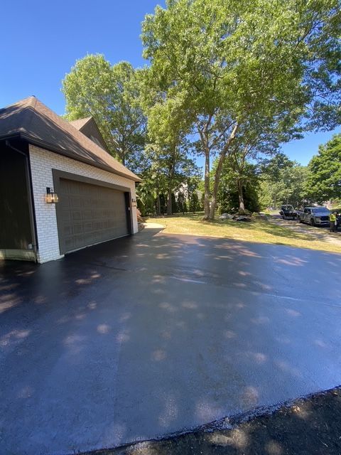 Wide driveway beside a garage and large trees on a sunny day