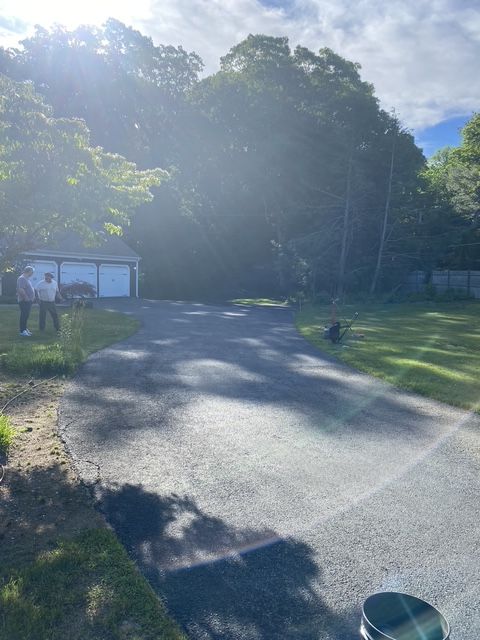 Sunlit gravel driveway beside trees, a white shed, and a parked truck in a rural yard