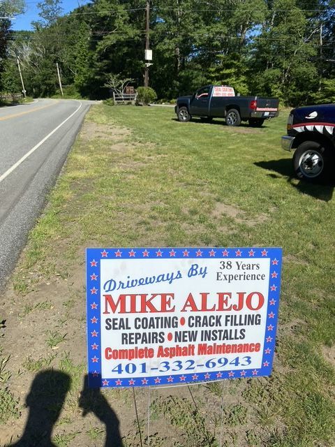 Political campaign sign for Mike Alejo on a roadside lawn beside a rural road and parked truck
