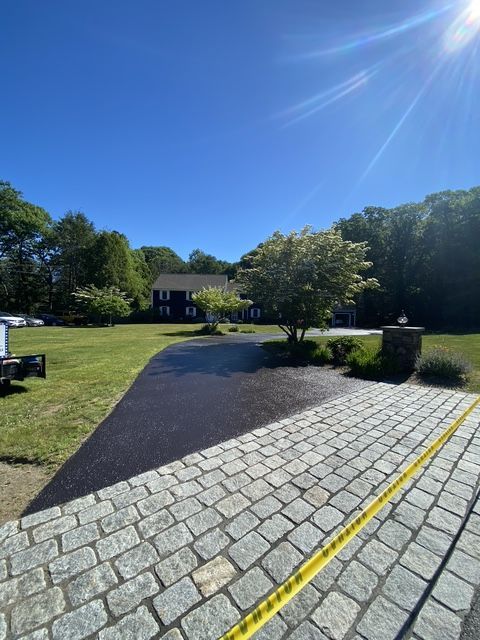 Sunny driveway with cobblestone edging leading to a house and lawn under a clear blue sky