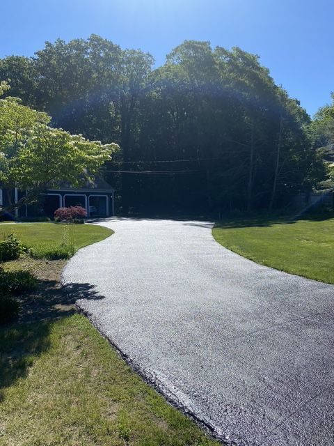 Curving paved path through a sunny green park with trees and a small building in the background