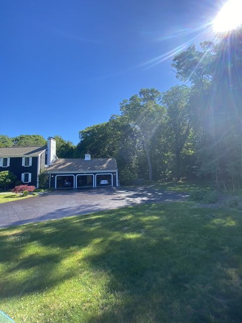 Suburban house with blue sky, sun glare, driveway, and green lawn bordered by trees
