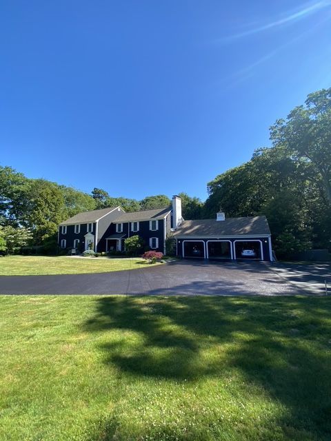 Suburban house with dark shutters, attached garage, and large green lawn under a clear blue sky