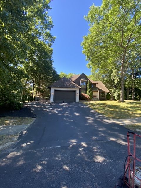Suburban house with a two-car garage, tree-lined driveway, and red bicycle on the right.