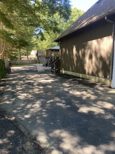 Shaded gravel path beside a wooden building, with trees and sunlight casting dappled shadows.