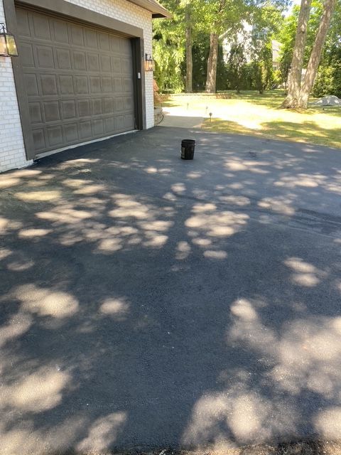 Driveway beside a garage with a black bucket in sunlight and tree shadows