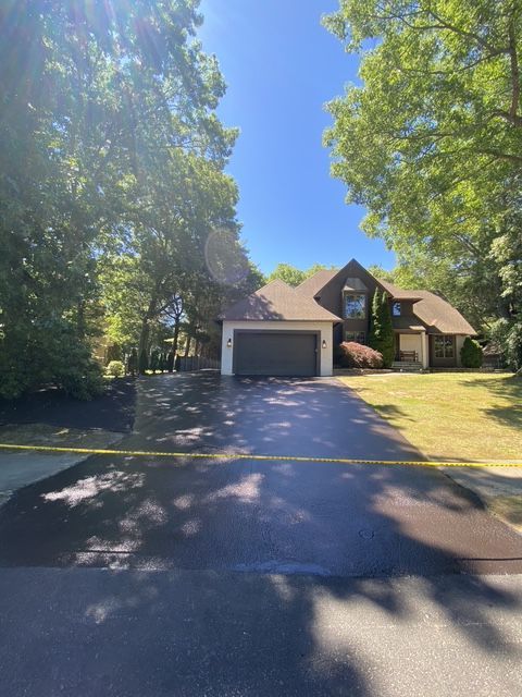 Suburban house with two-car garage, trees framing the driveway, and bright sunlight on the front lawn