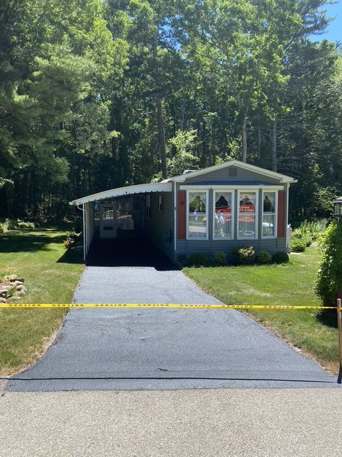 Small gray cottage with a driveway, set among trees in a wooded area.
