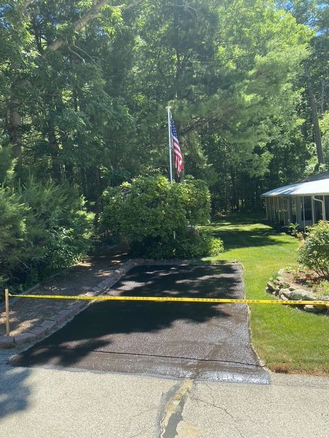 Blocked driveway with yellow caution tape, an American flag, and a house beside a wooded yard.