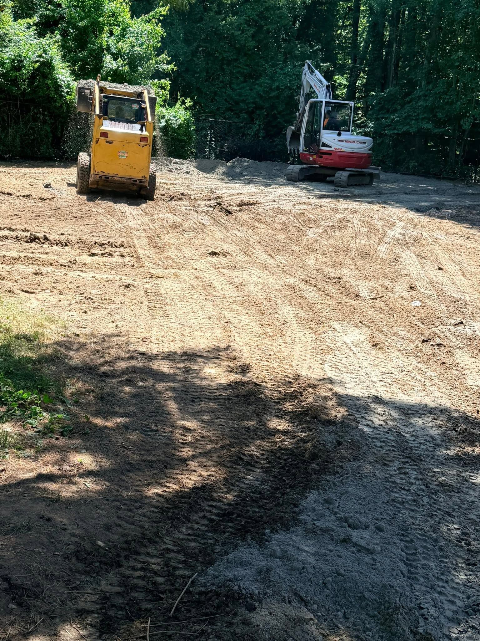 Two construction machines on a dirt path in a wooded area, one yellow and one red-white.