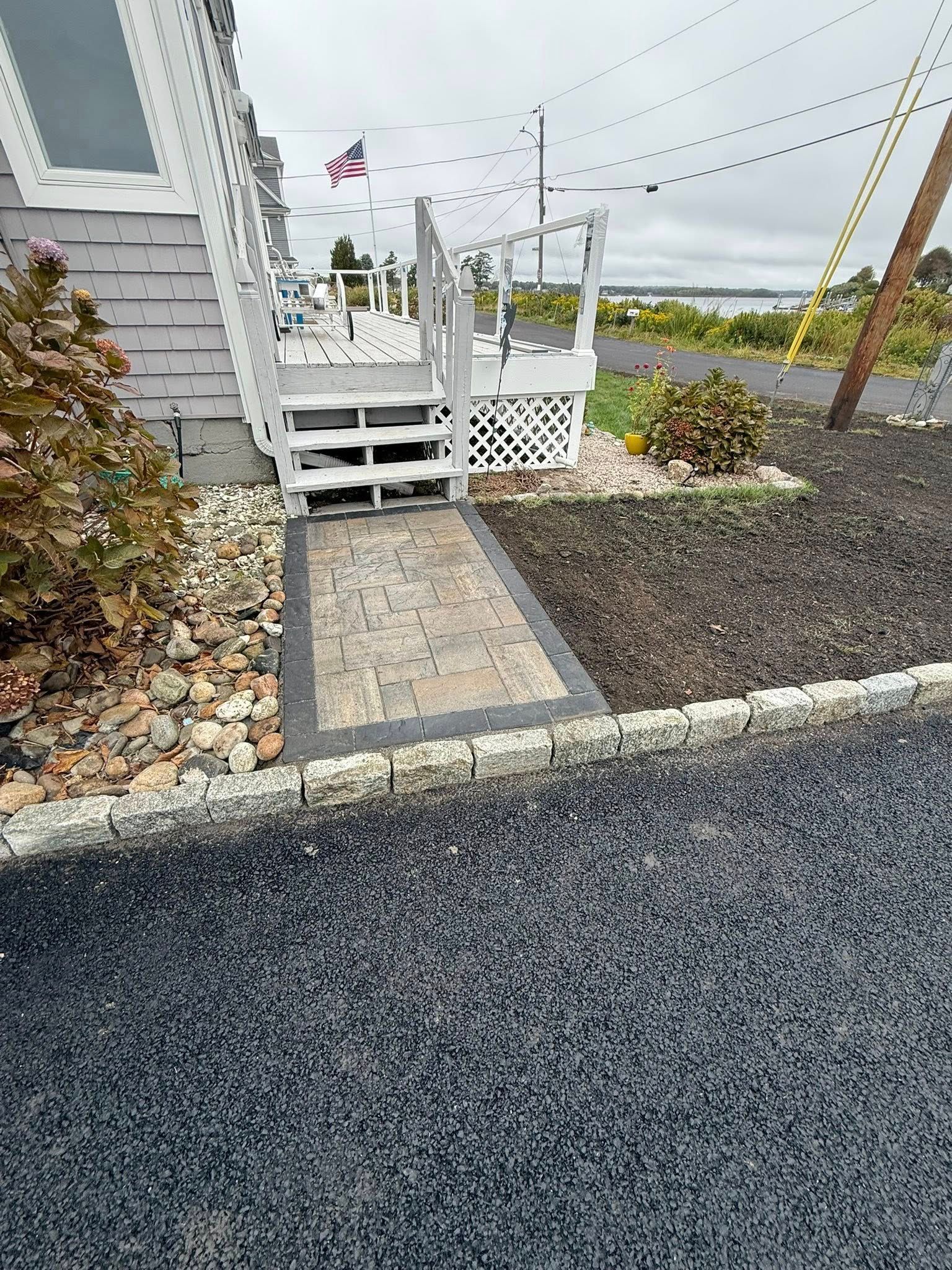 White stairs leading to a deck entrance, featuring a paved walkway bordered by cobblestones and gravel landscaping.