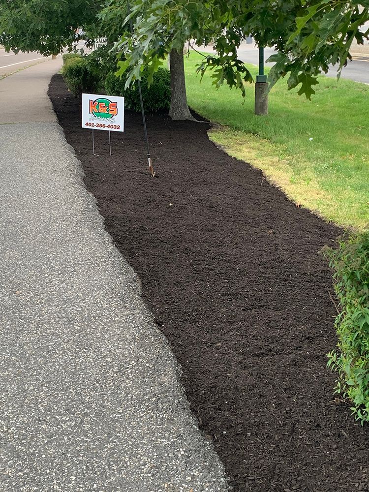 A sign is sitting on the side of a road next to a row of mulch.