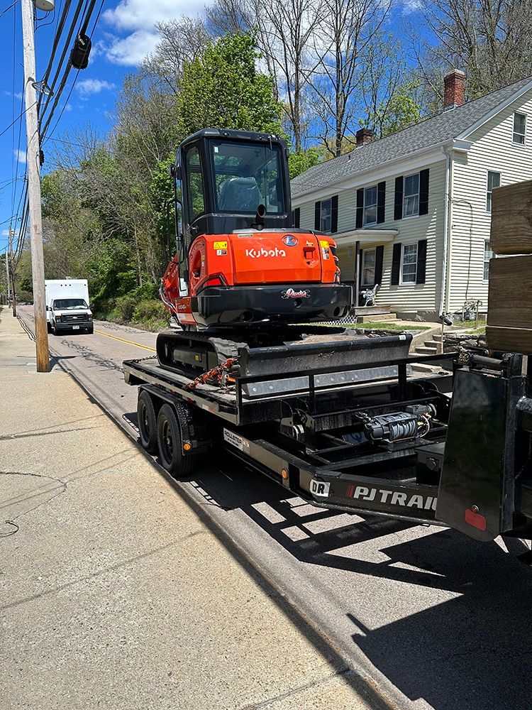 A small excavator is being towed on a trailer down a street.